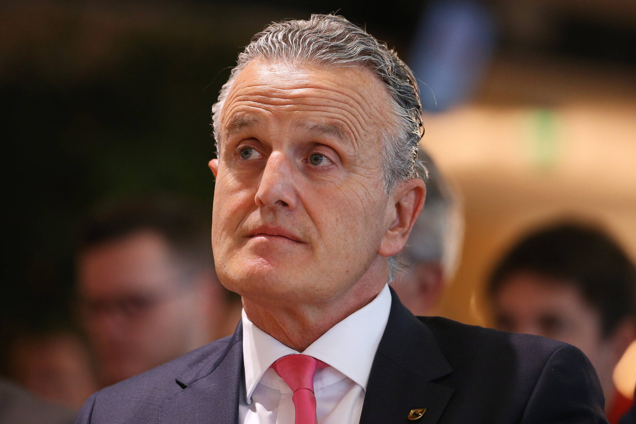 Ein Mann in Anzug und Krawatte schaut zur Seite. Hintergrund unscharf.