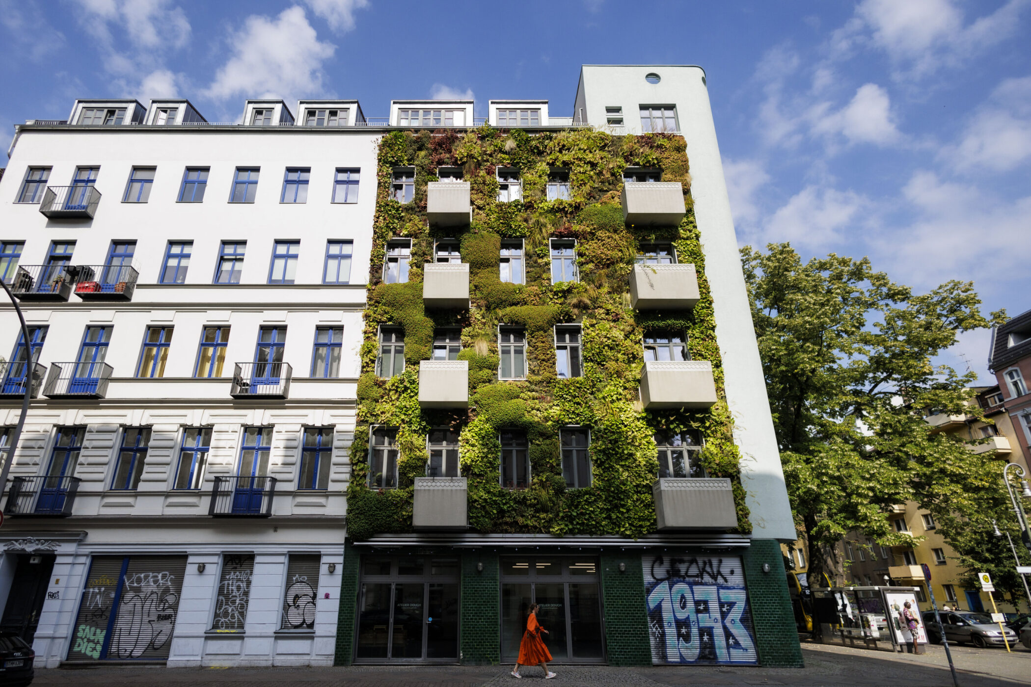 Fassade eines Gebäudes mit vertikalem Garten, Balkonen und Graffiti. Eine Person geht vorbei.