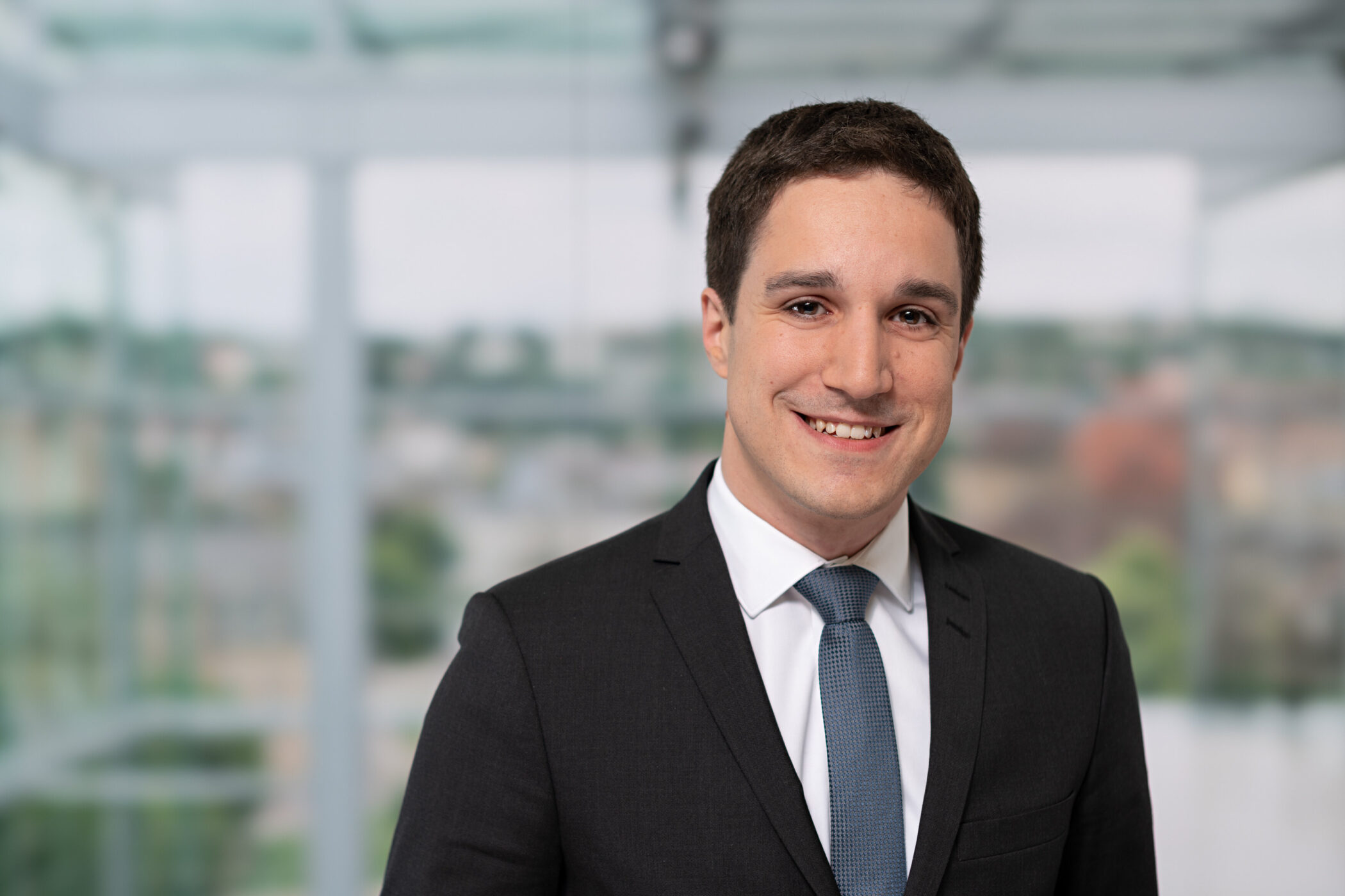 Ein Mann im Anzug lächelt vor unscharfem Hintergrund.