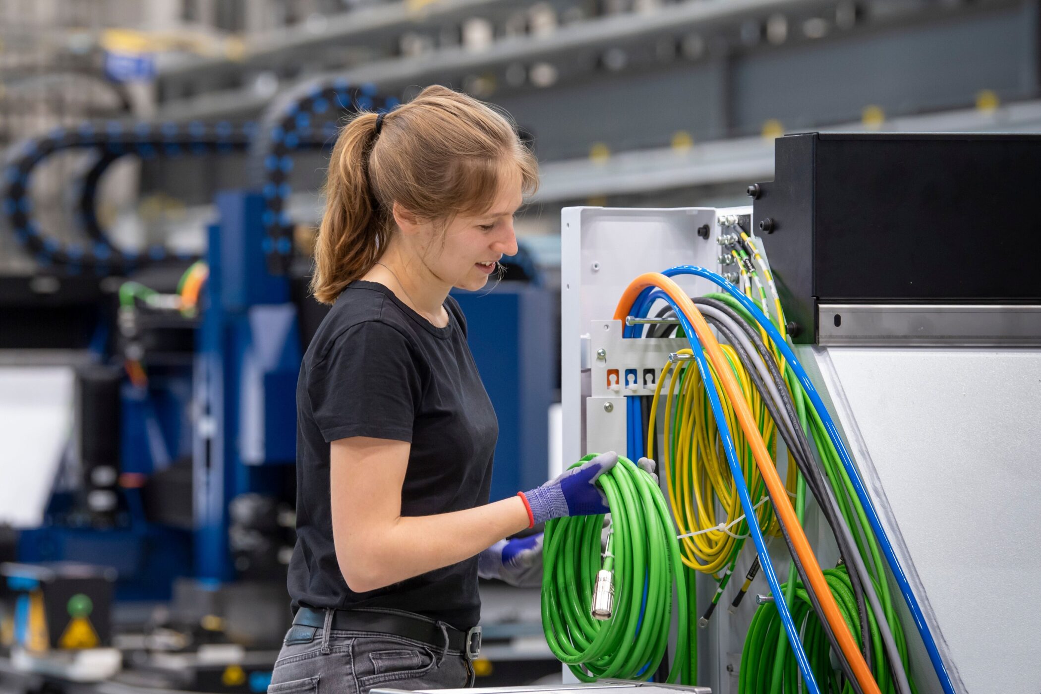 Frau in Werkstatt arbeitet mit bunten Kabeln an einer Maschine.