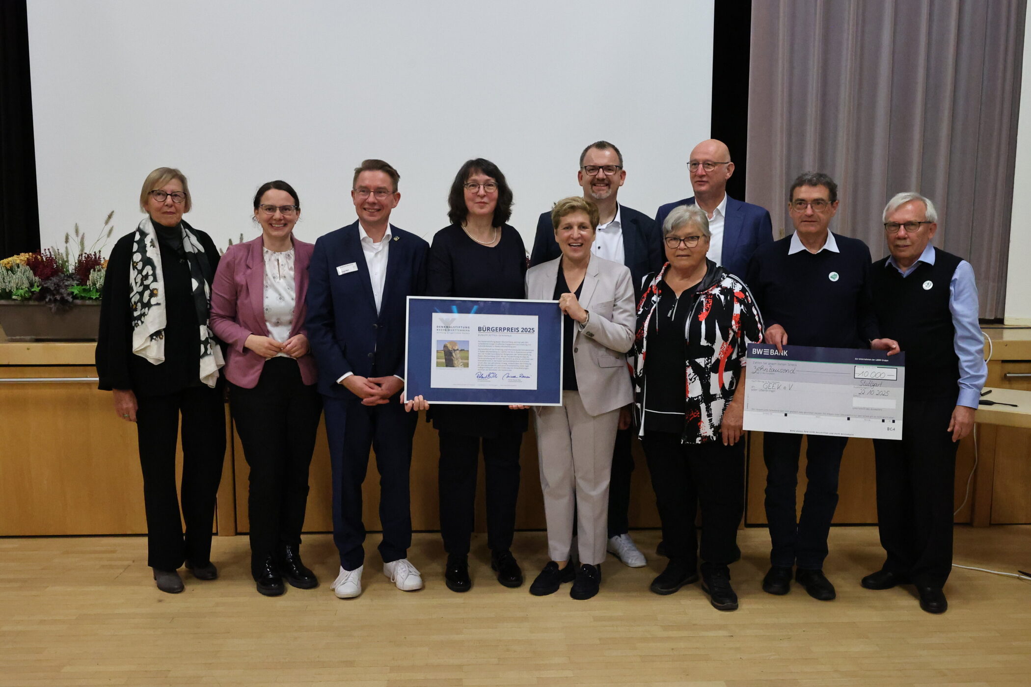 Zehn Personen stehen zusammen, zwei halten Urkunde und Scheck.