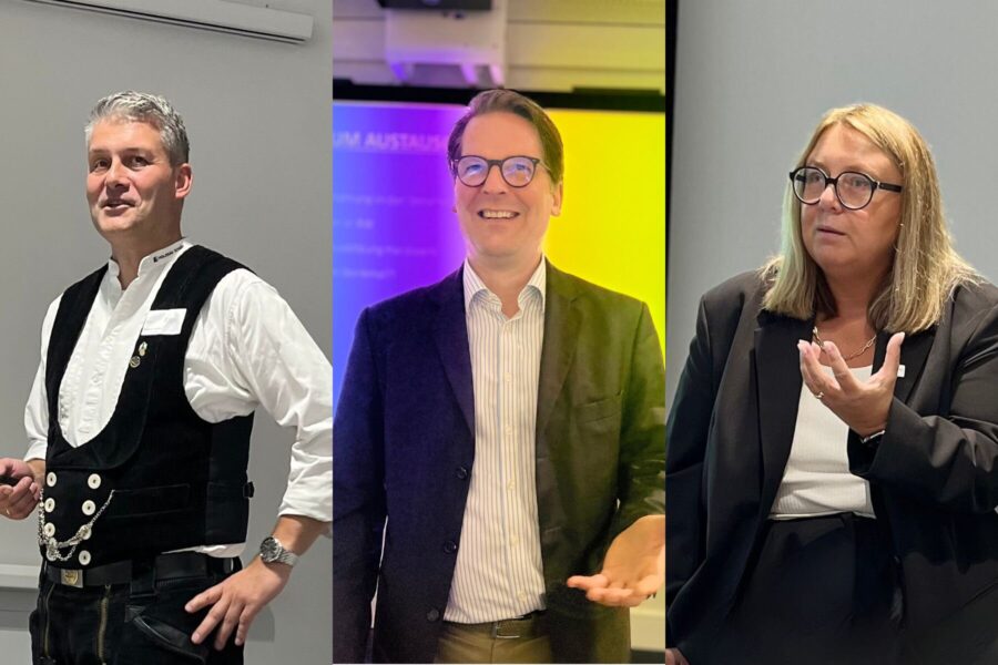 Drei Personen in formeller Kleidung sprechen vor Publikum.