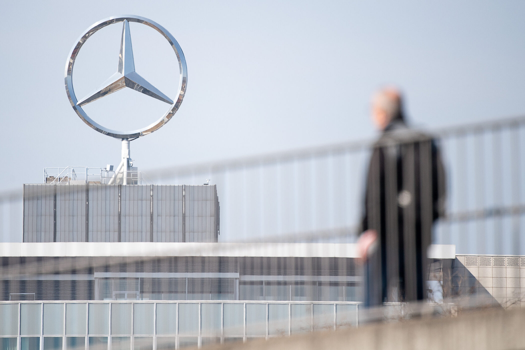 Gebäude mit großem Mercedes-Logo, unscharfe Person im Vordergrund.