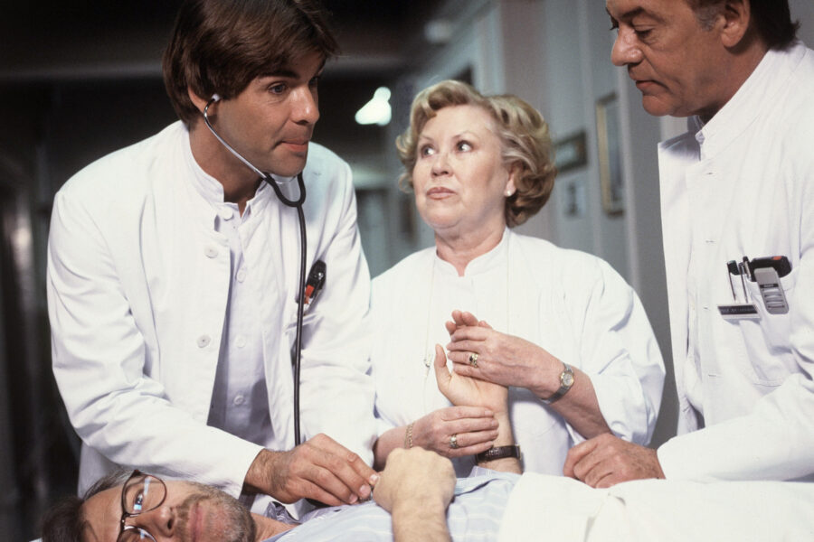 Drei Ärzte untersuchen einen Patienten im Krankenhausbett.