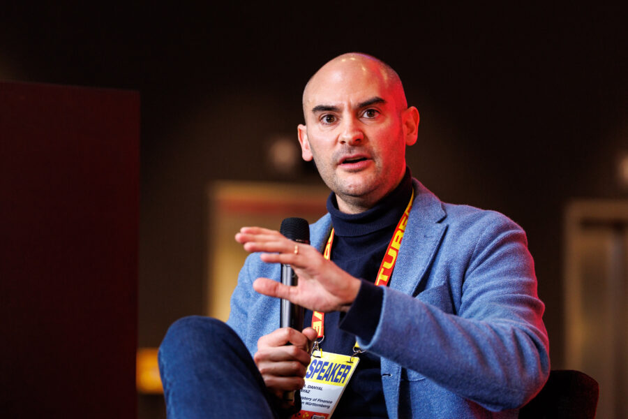 Ein Mann mit Mikrofon und Namensschild spricht gestikulierend.