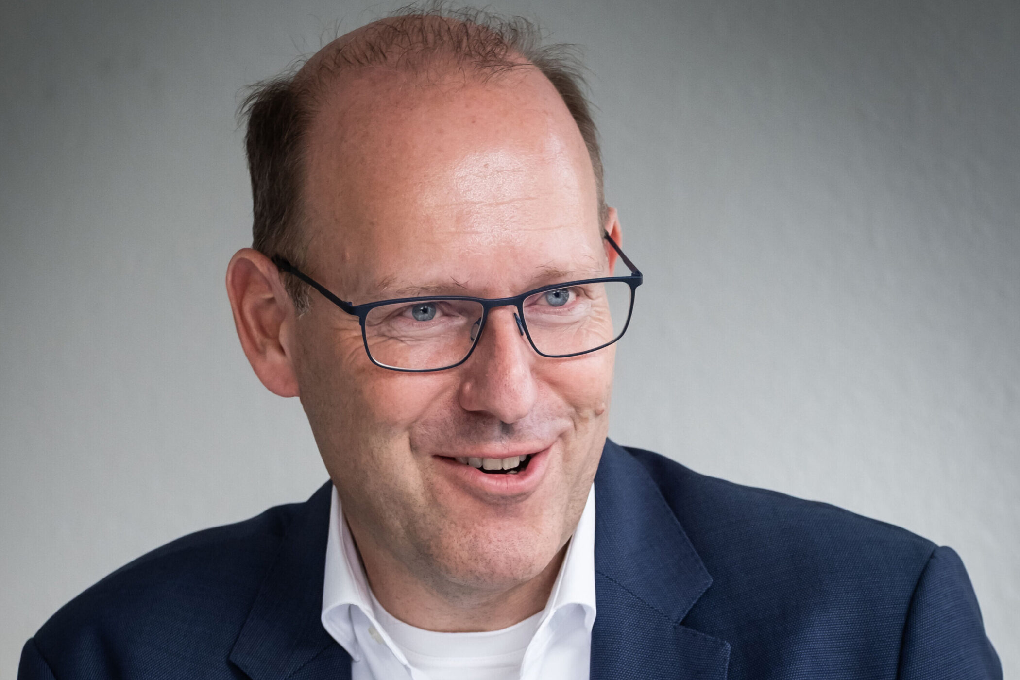 Ein Mann mit Brille und Anzug lächelt.