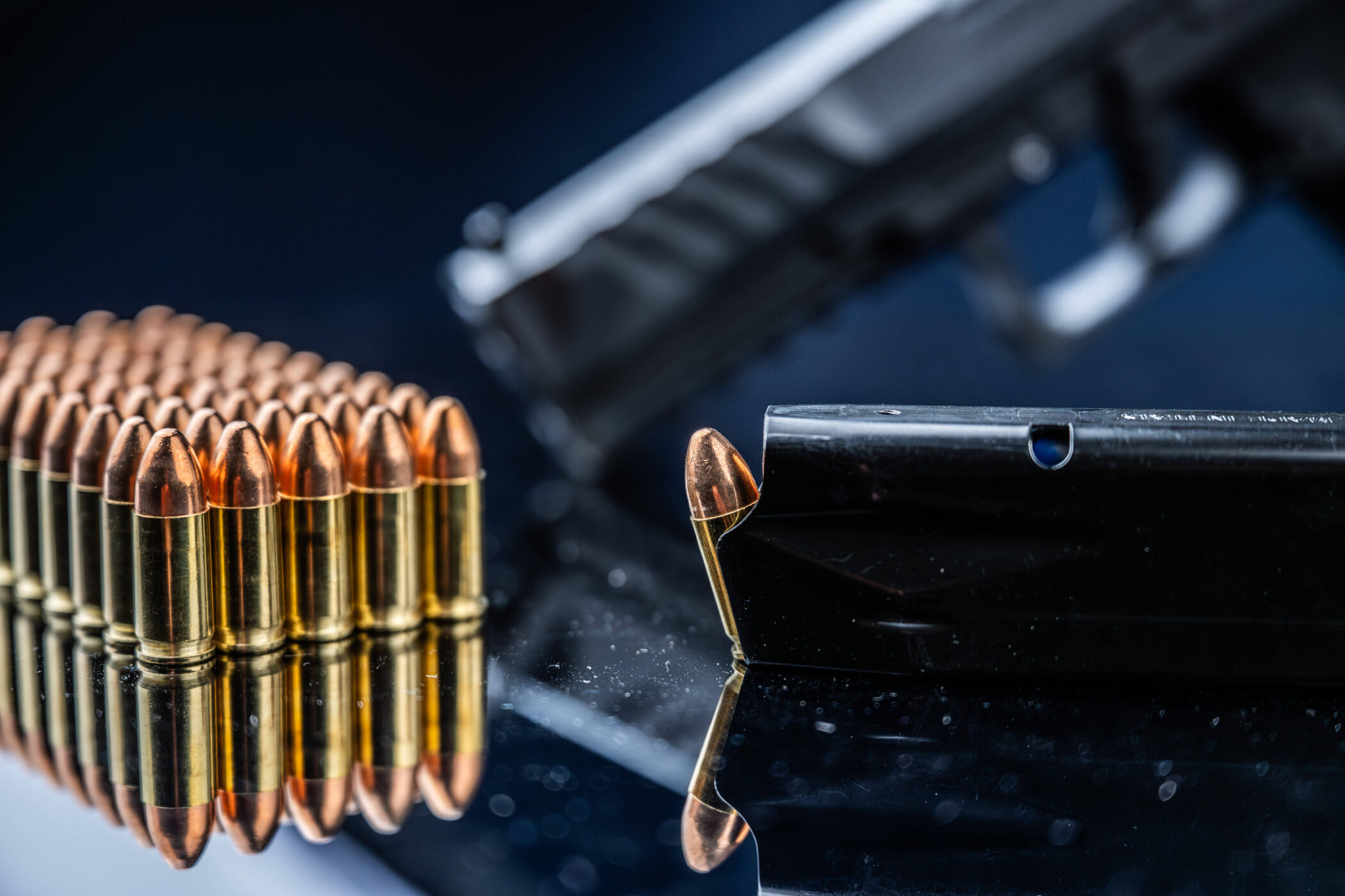 Reihe von Patronen, Magazin und unscharfe Pistole auf reflektierender Oberfläche.