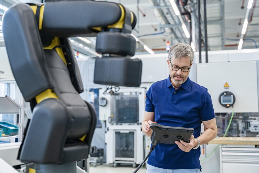 Mann in Werkstatt bedient Roboterarm mit Steuergerät.