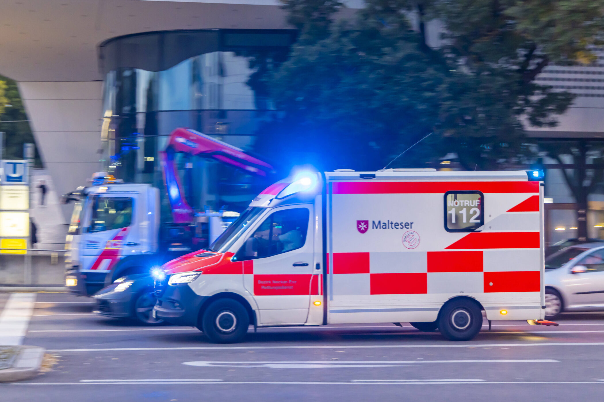 Krankenwagen mit Blaulicht fährt auf Straße, daneben ein weiteres Fahrzeug.