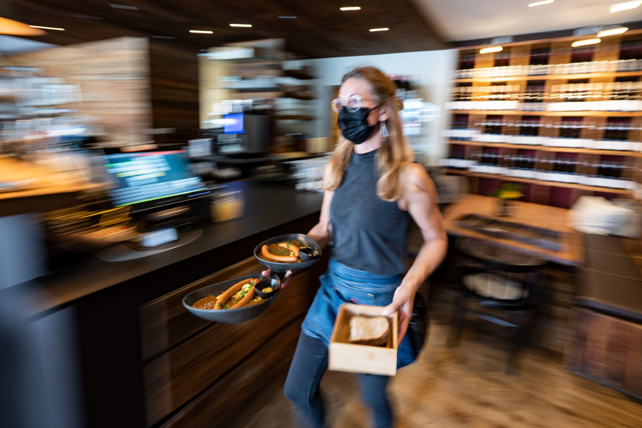 Person mit Maske serviert Essen in einem Restaurant.