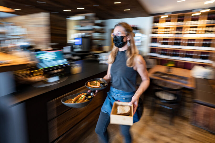 Person mit Maske serviert Essen in einem Restaurant.