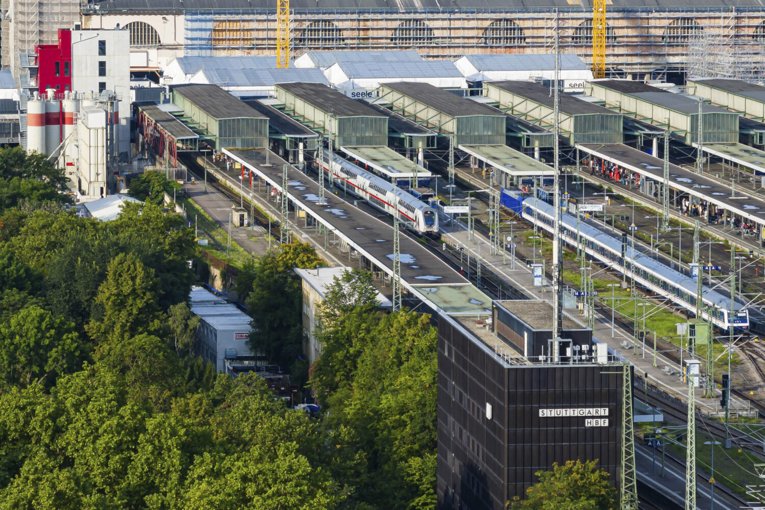 Bahnhof mit mehreren Gleisen, Zügen und Menschen. Gebäude mit "Stuttgart Hbf" Schild.
