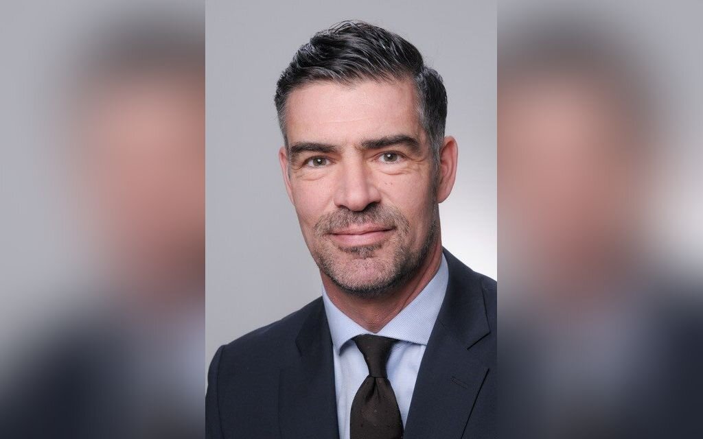 Ein Mann in Anzug und Krawatte vor grauem Hintergrund.