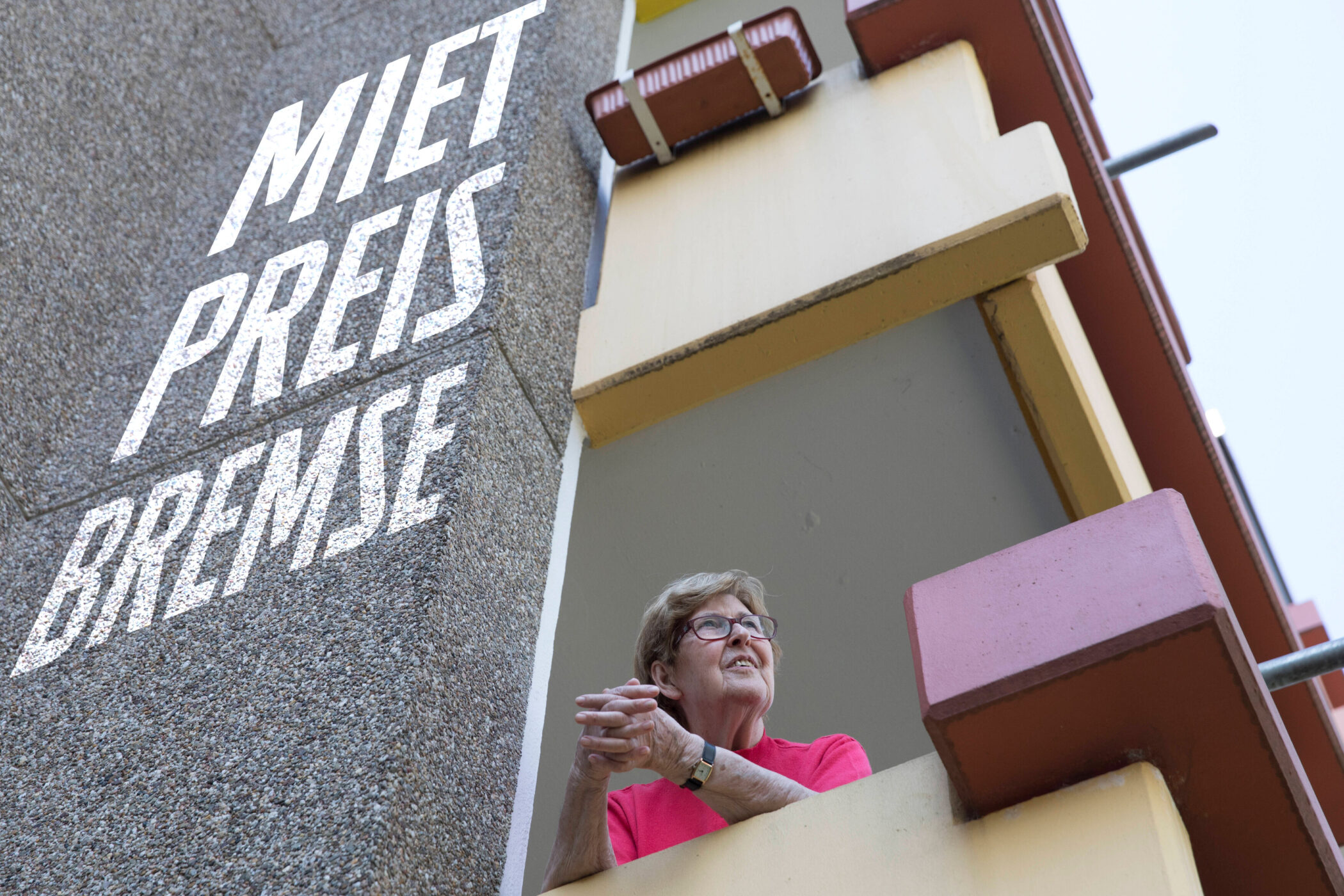Ältere Frau steht auf Balkon, daneben Schriftzug "MIET PREIS BREMSE".