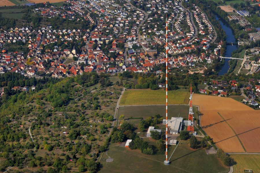 Stadtansicht mit vielen Häusern, Fluss, Feldern und einem hohen Sendemast.