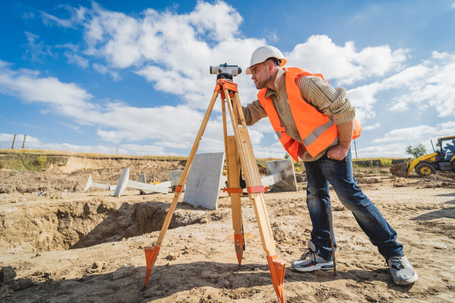 Mann mit Helm und Weste nutzt Vermessungsgerät auf Baustelle.