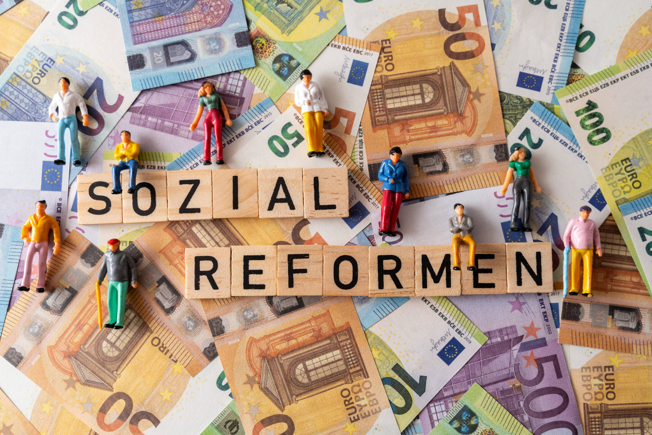 Miniaturfiguren auf Euro-Scheinen, Scrabble-Steine bilden "SOZIAL REFORMEN".