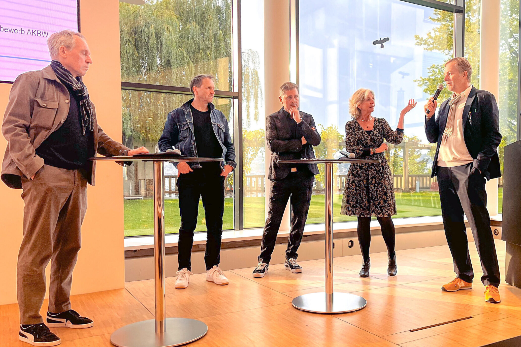 Fünf Personen stehen an Stehtischen, eine Person spricht ins Mikrofon.