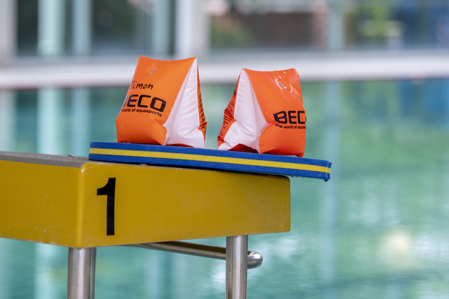 Zwei orange Schwimmflügel auf einem gelben Startblock mit der Nummer 1.