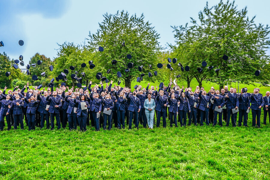 Gruppe von Menschen in Uniformen wirft Hüte in die Luft, im Freien auf einer Wiese.