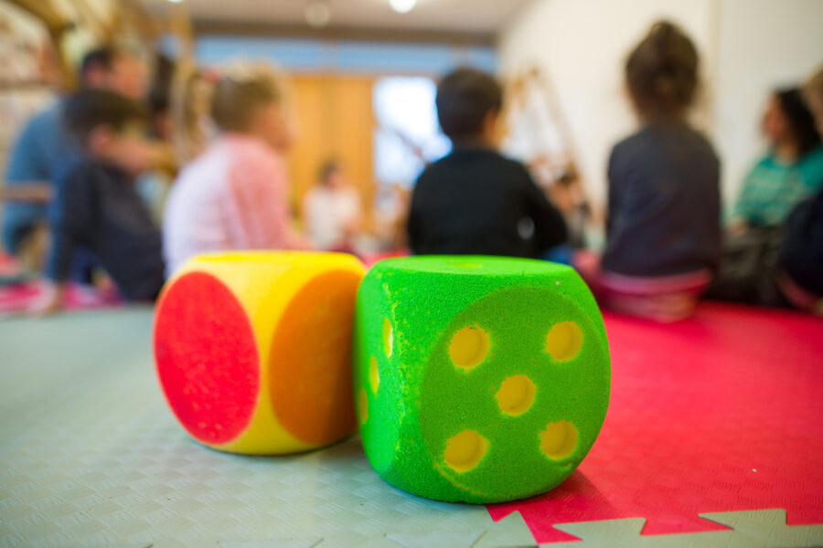 Zwei bunte Schaumstoffwürfel im Vordergrund, unscharfe Kinder im Hintergrund.