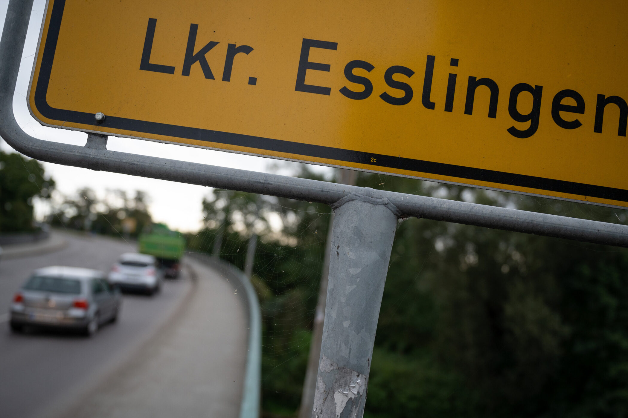Gelbes Schild mit der Aufschrift "Lkr. Esslingen", Straße mit Autos im Hintergrund.