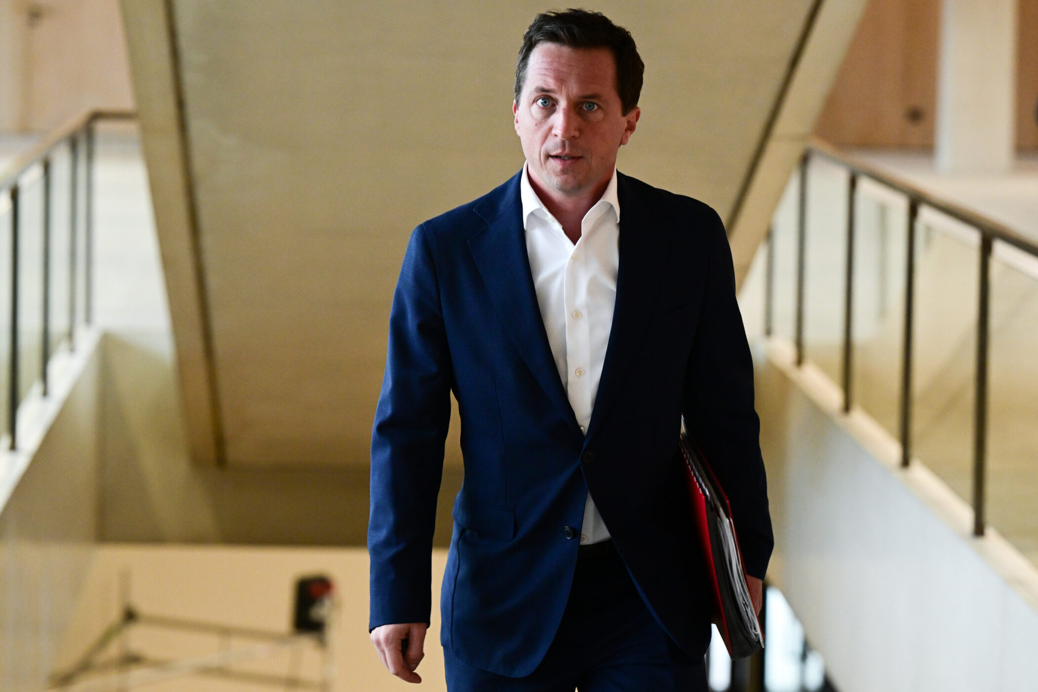 Mann in Anzug geht Treppe hinauf, hält rote Mappe in der Hand.