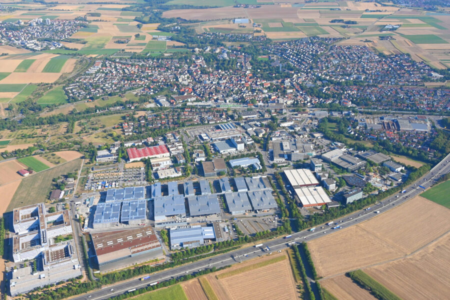 Luftaufnahme einer Stadt mit Wohngebieten, Feldern und Industrieanlagen.