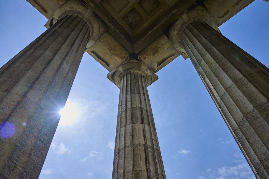 Drei steinerne Säulen von unten, blauer Himmel und Sonne im Hintergrund.