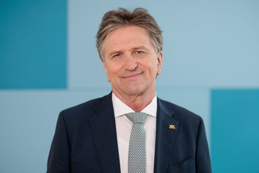 Mann in Anzug mit gemusterter Krawatte vor blauem Hintergrund.