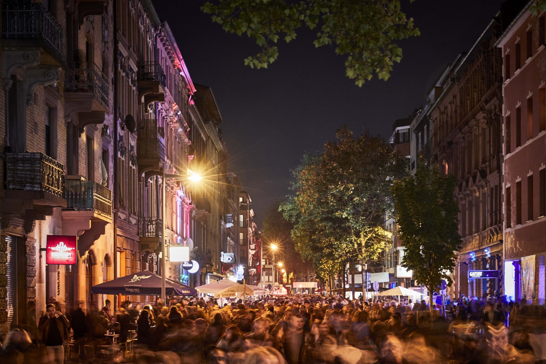 Belebte Straße bei Nacht mit Menschenmenge und beleuchteten Gebäuden.