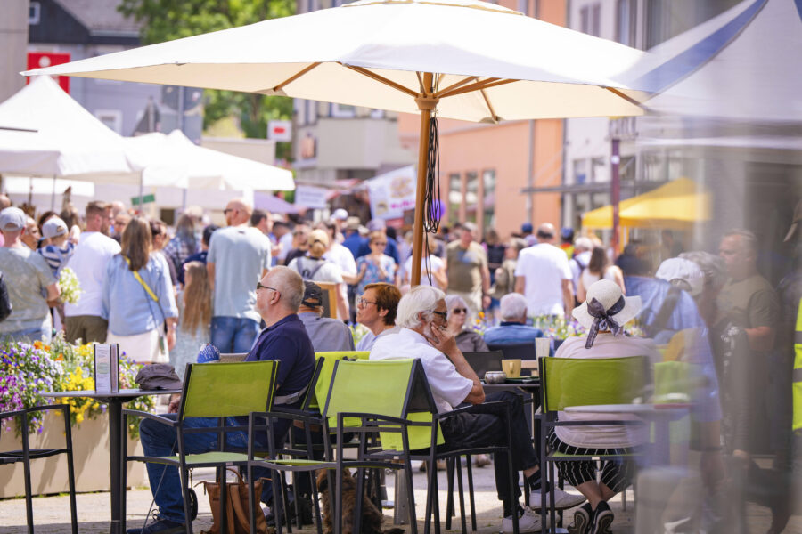 Menschen sitzen unter Sonnenschirmen in einem belebten Straßencafé.
