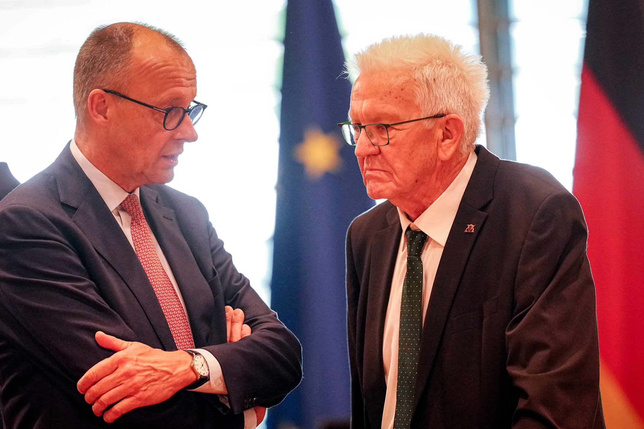 Zwei Männer im Anzug im Gespräch, im Hintergrund Flaggen.