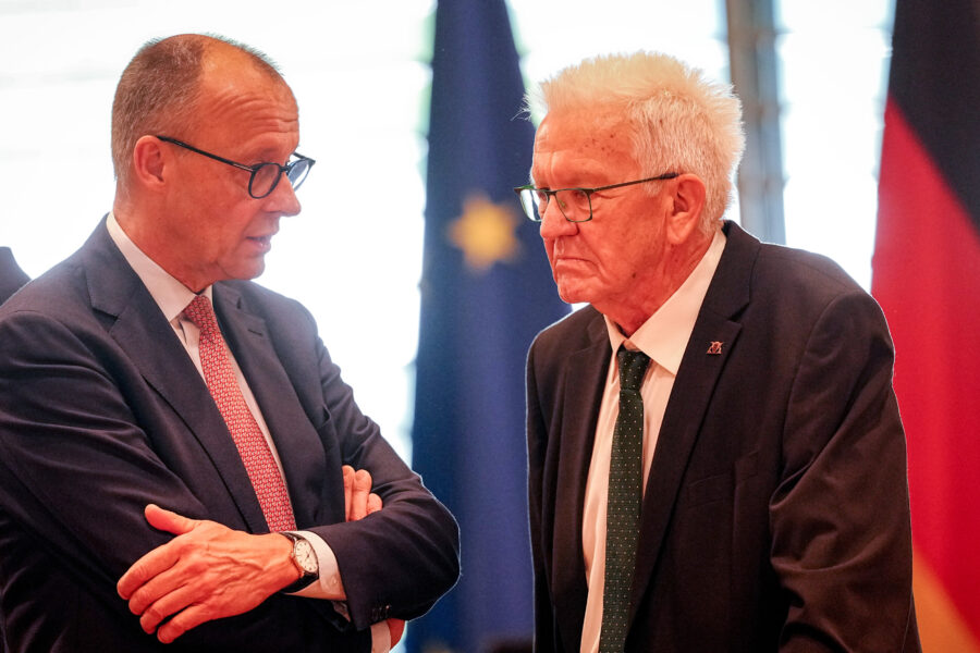 Zwei Männer im Anzug im Gespräch, im Hintergrund Flaggen.