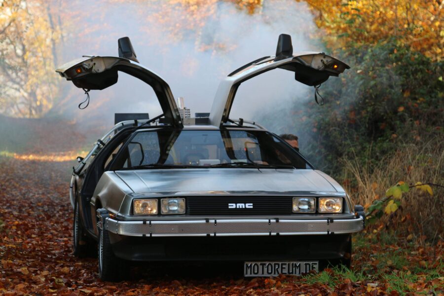 Auto mit Flügeltüren auf Waldweg, Herbstlaub, Kennzeichen "MOTOREUM.DE".