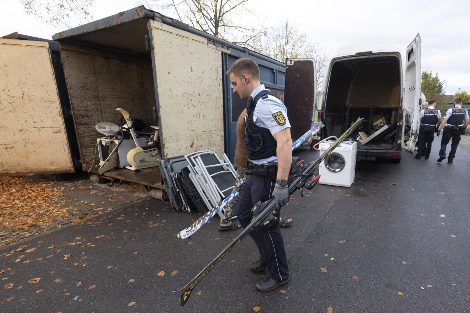 Polizist trägt Skier, neben ihm ein geöffneter Container mit Fitnessgerät.