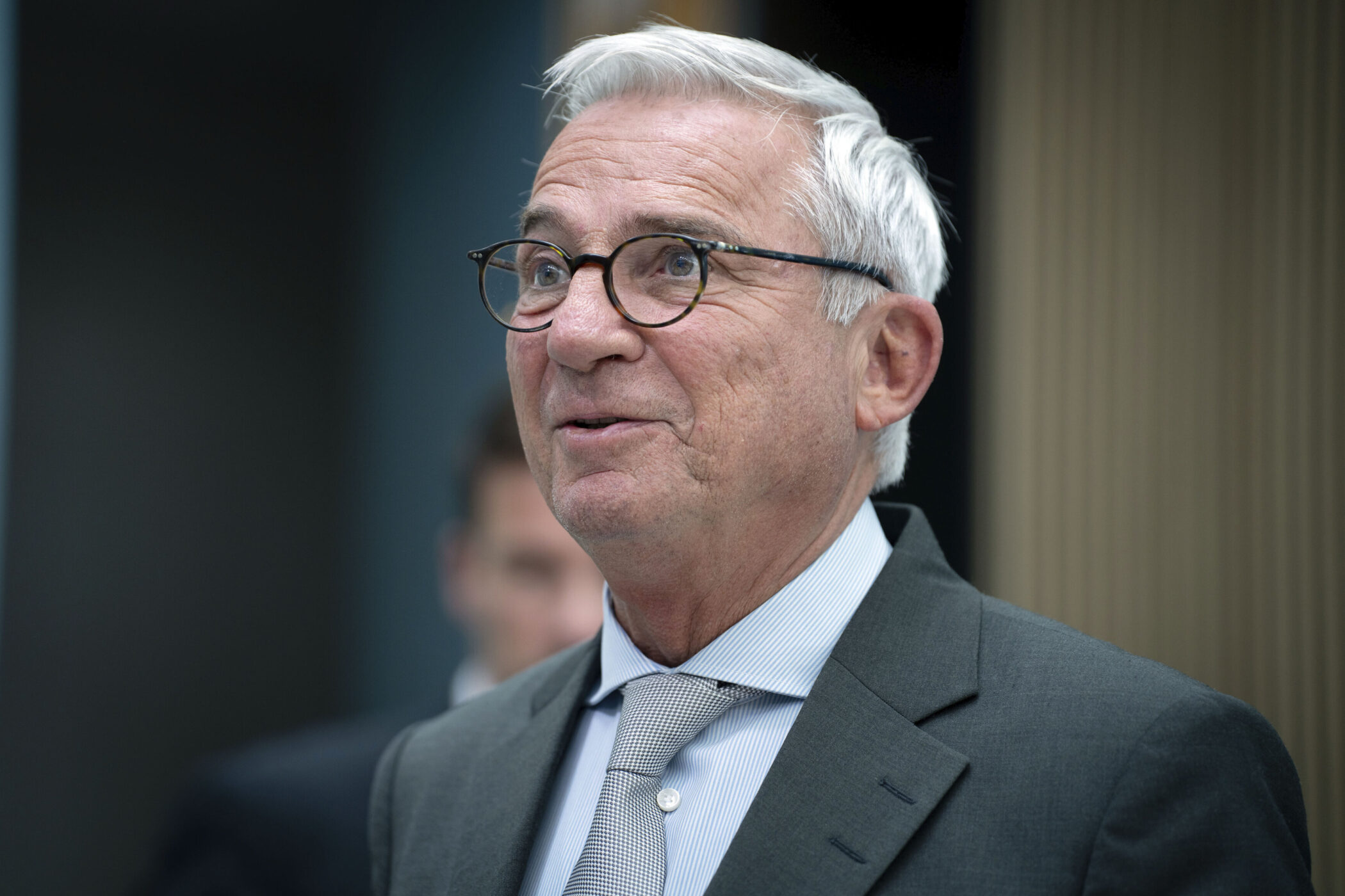 Älterer Mann mit Brille und grauem Anzug, lächelnd.