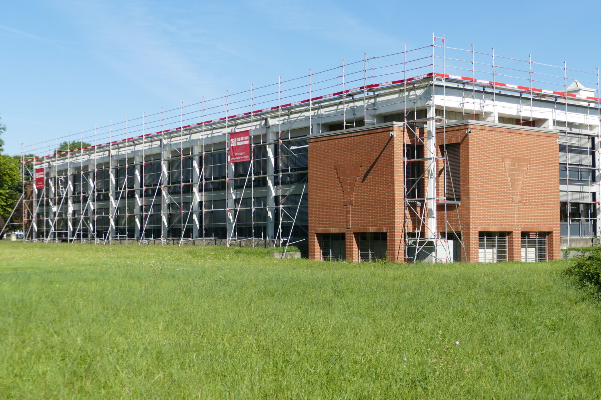Gebäude mit Gerüst, rote Ziegelwand, grüne Wiese im Vordergrund.