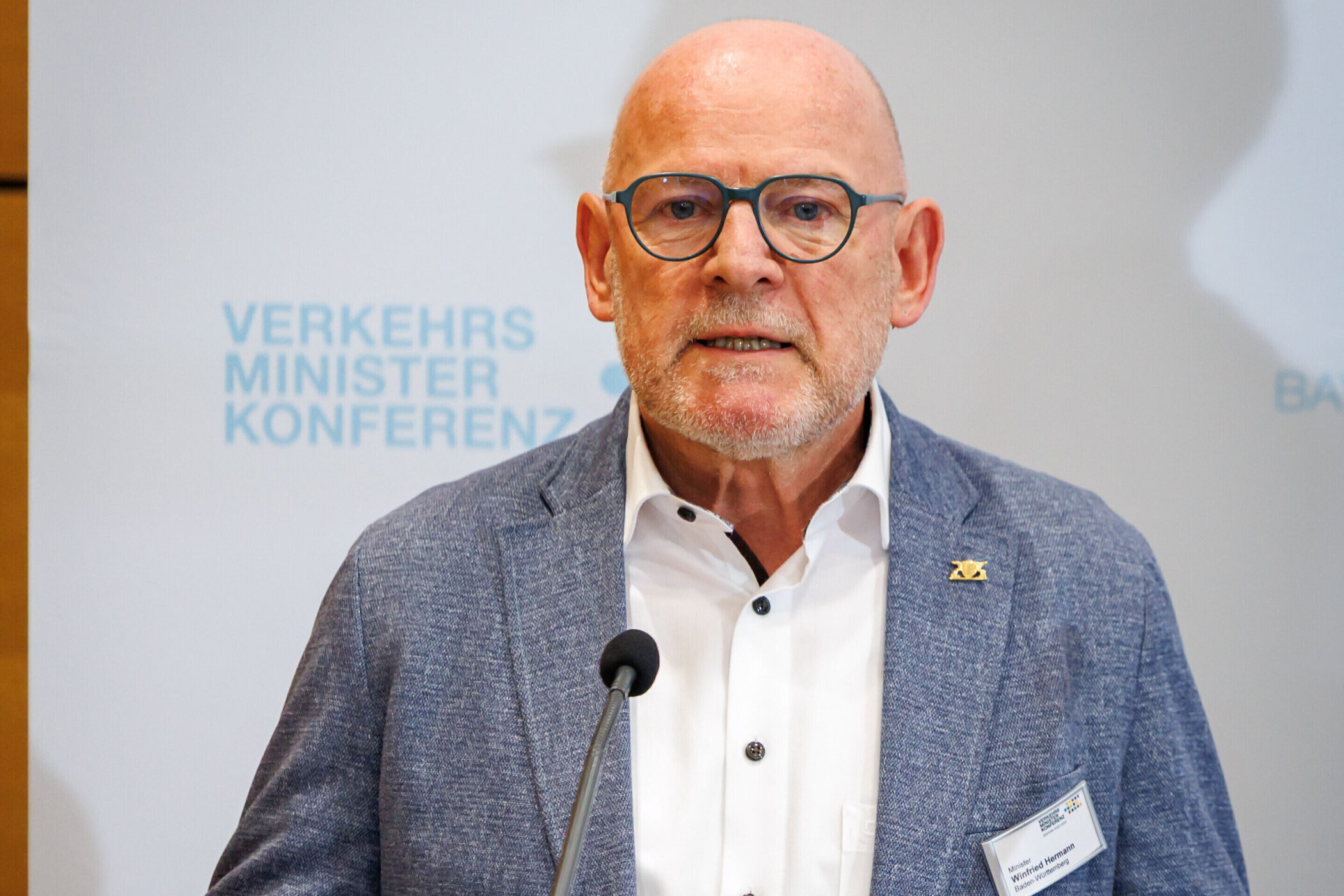 Älterer Mann mit Brille spricht vor Mikrofon, Hintergrundtext: "Verkehrsministerkonferenz".
