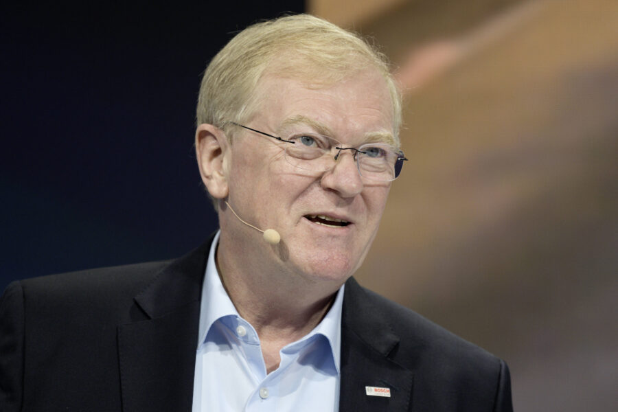 Älterer Mann mit Brille und Mikrofon, trägt Anzug mit Bosch-Logo.