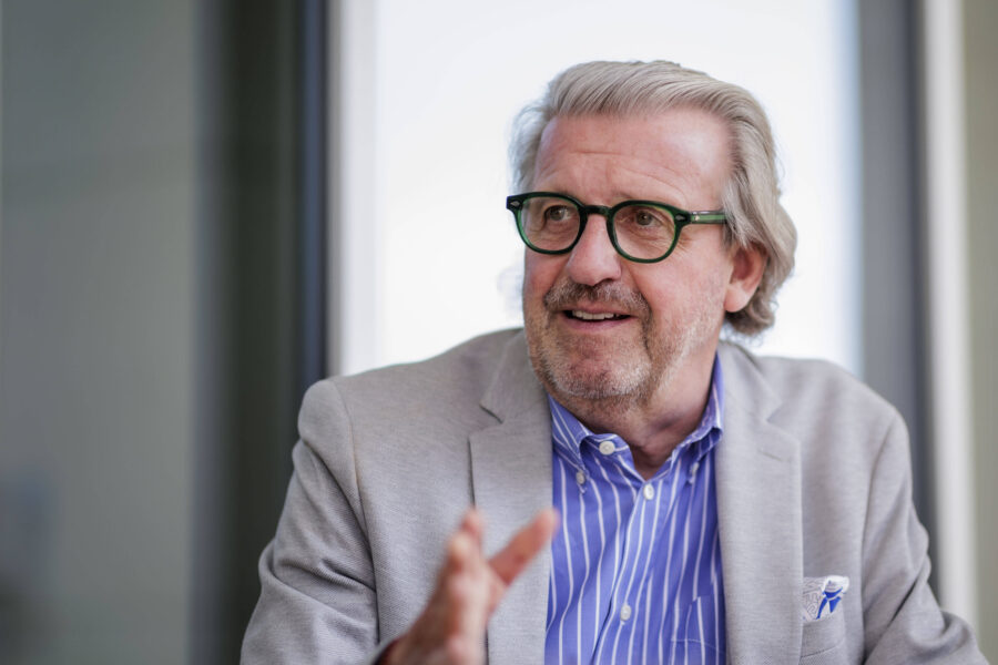 Älterer Mann mit Brille und grauem Sakko gestikuliert im Gespräch.