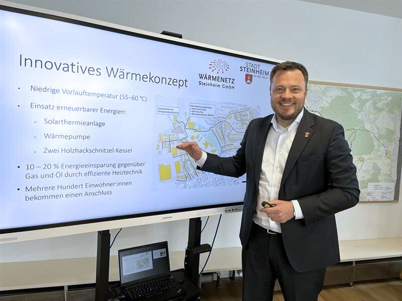 Mann im Anzug präsentiert ein Wärmekonzept auf einem Bildschirm mit Karte und Text.