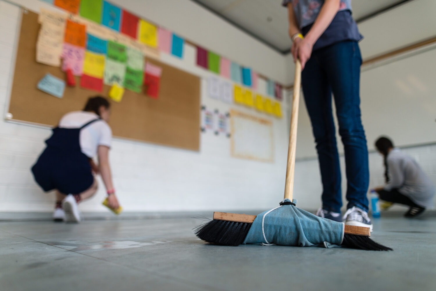 Drei Personen reinigen einen Raum mit Besen und Tüchern.