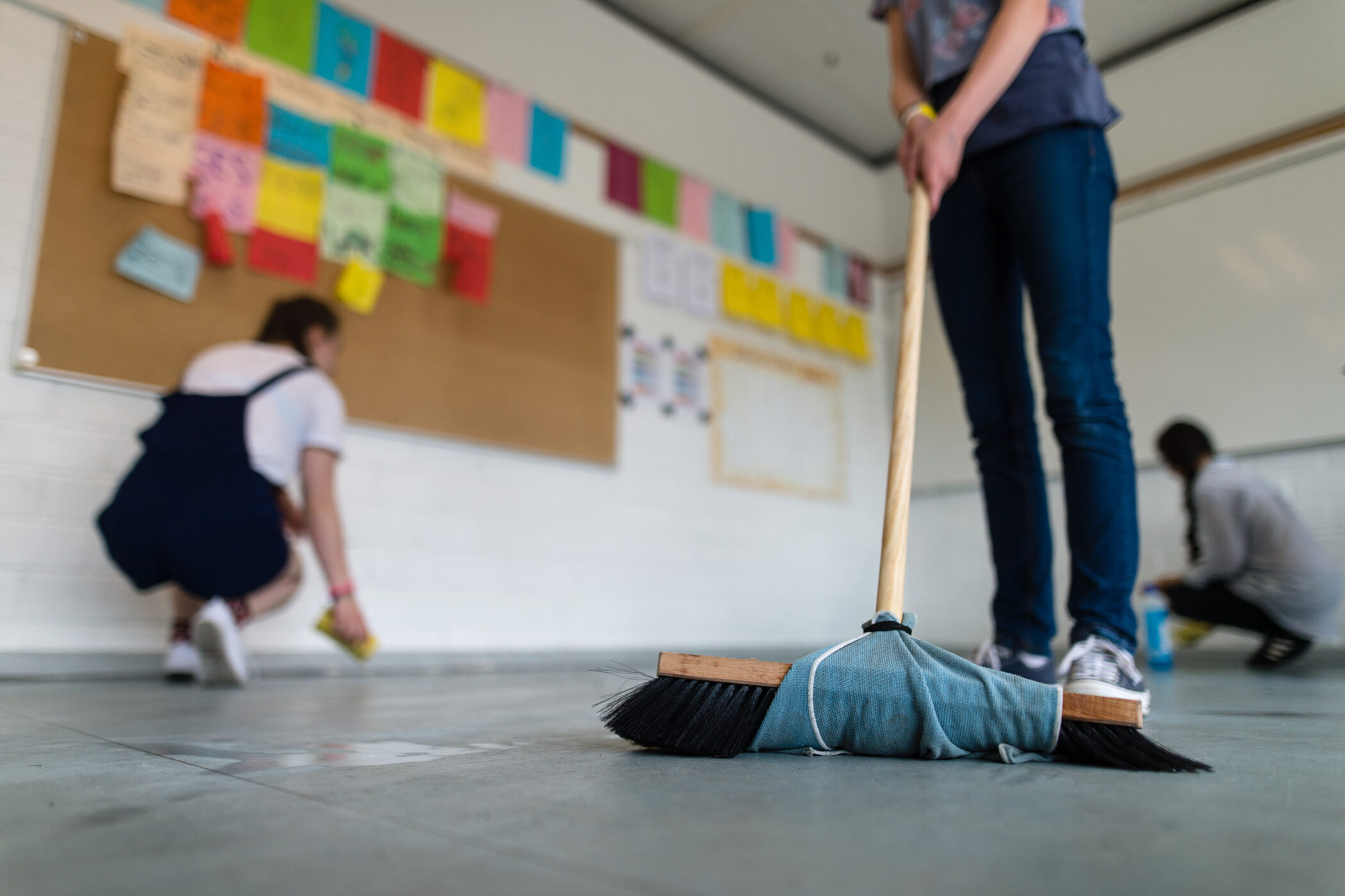 Drei Personen reinigen einen Raum mit Besen und Tüchern.