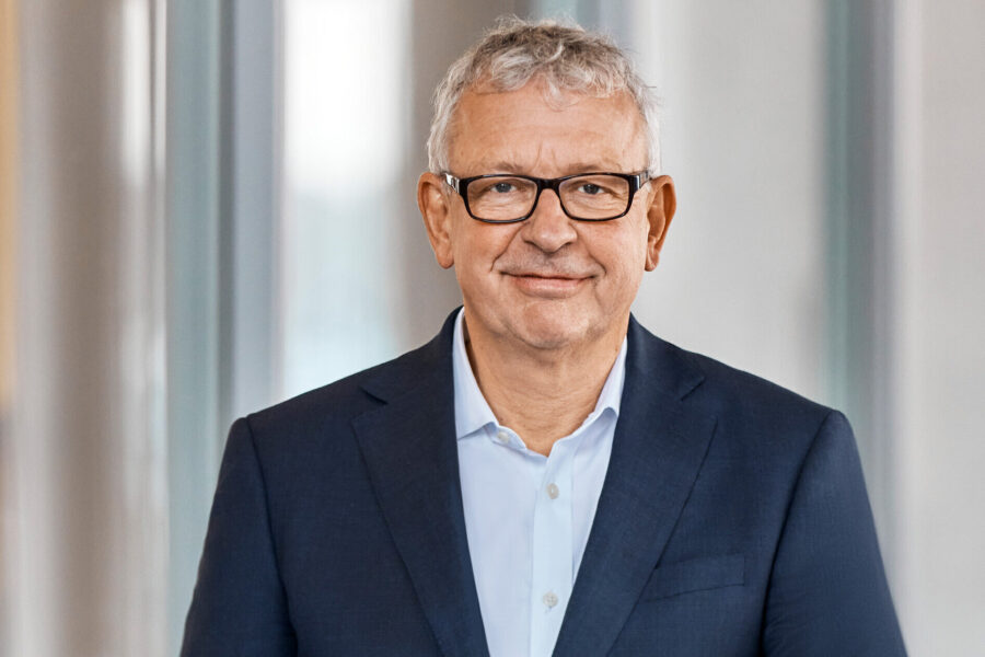 Älterer Mann mit Brille und Anzug lächelt in die Kamera.