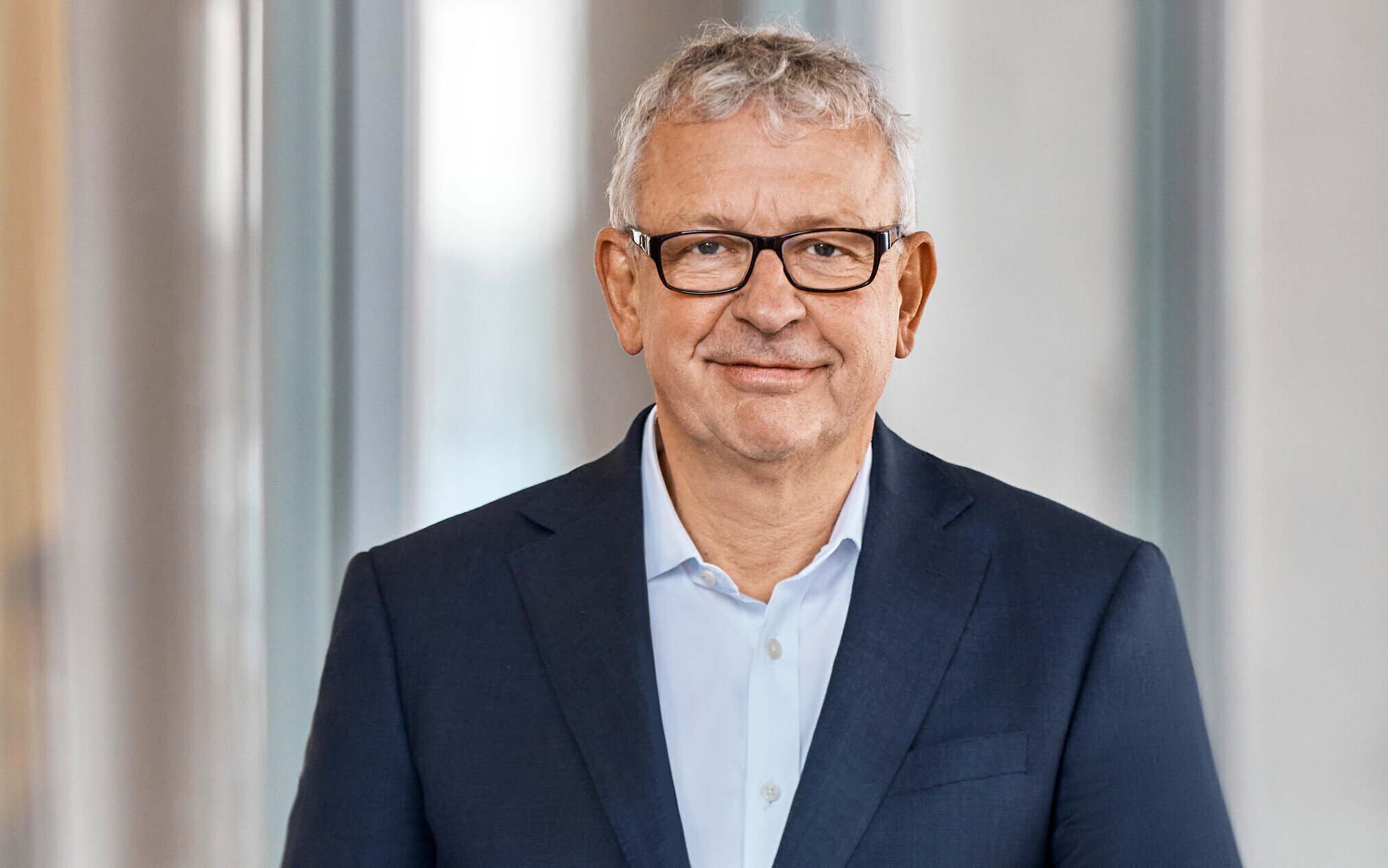 Älterer Mann mit Brille und Anzug lächelt in die Kamera.