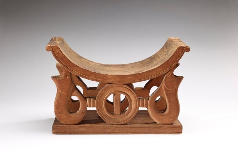 Holzhocker mit geschwungener Sitzfläche und dekorativen, geschnitzten Beinen.