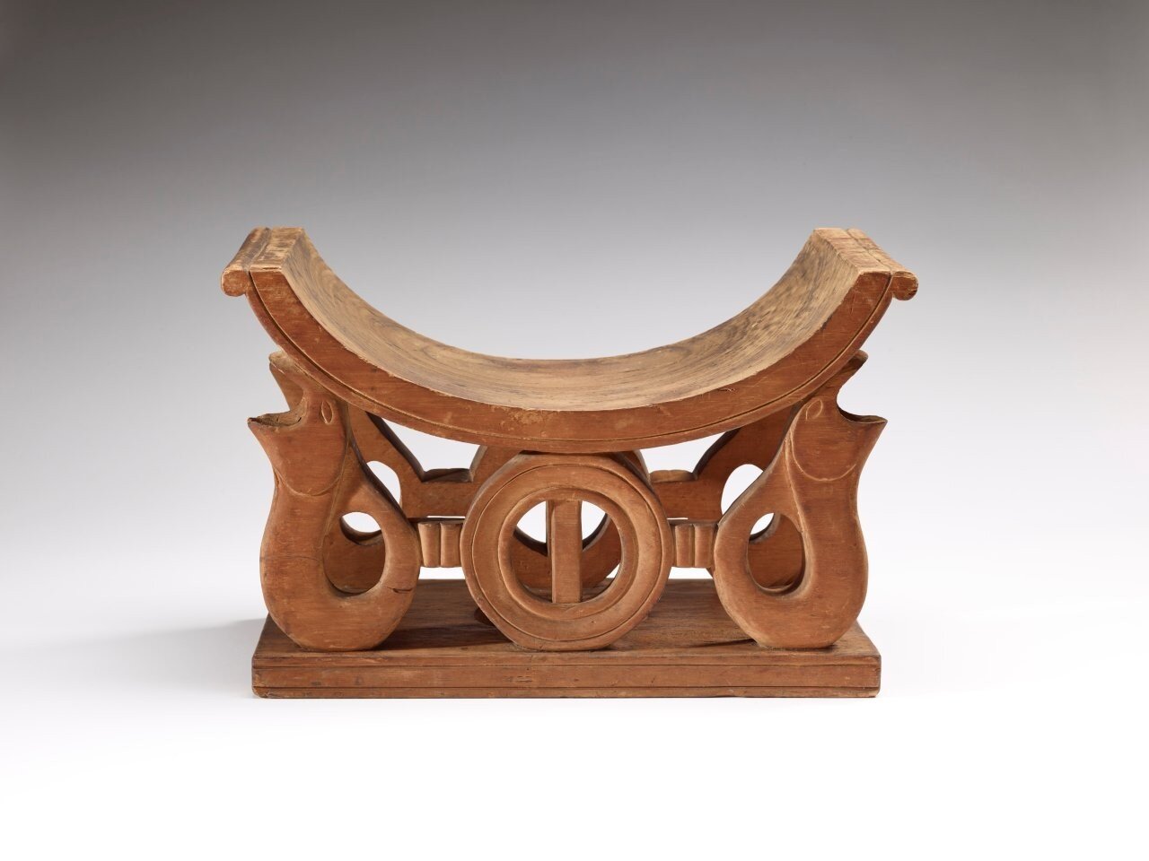 Holzhocker mit geschwungener Sitzfläche und dekorativen, geschnitzten Beinen.