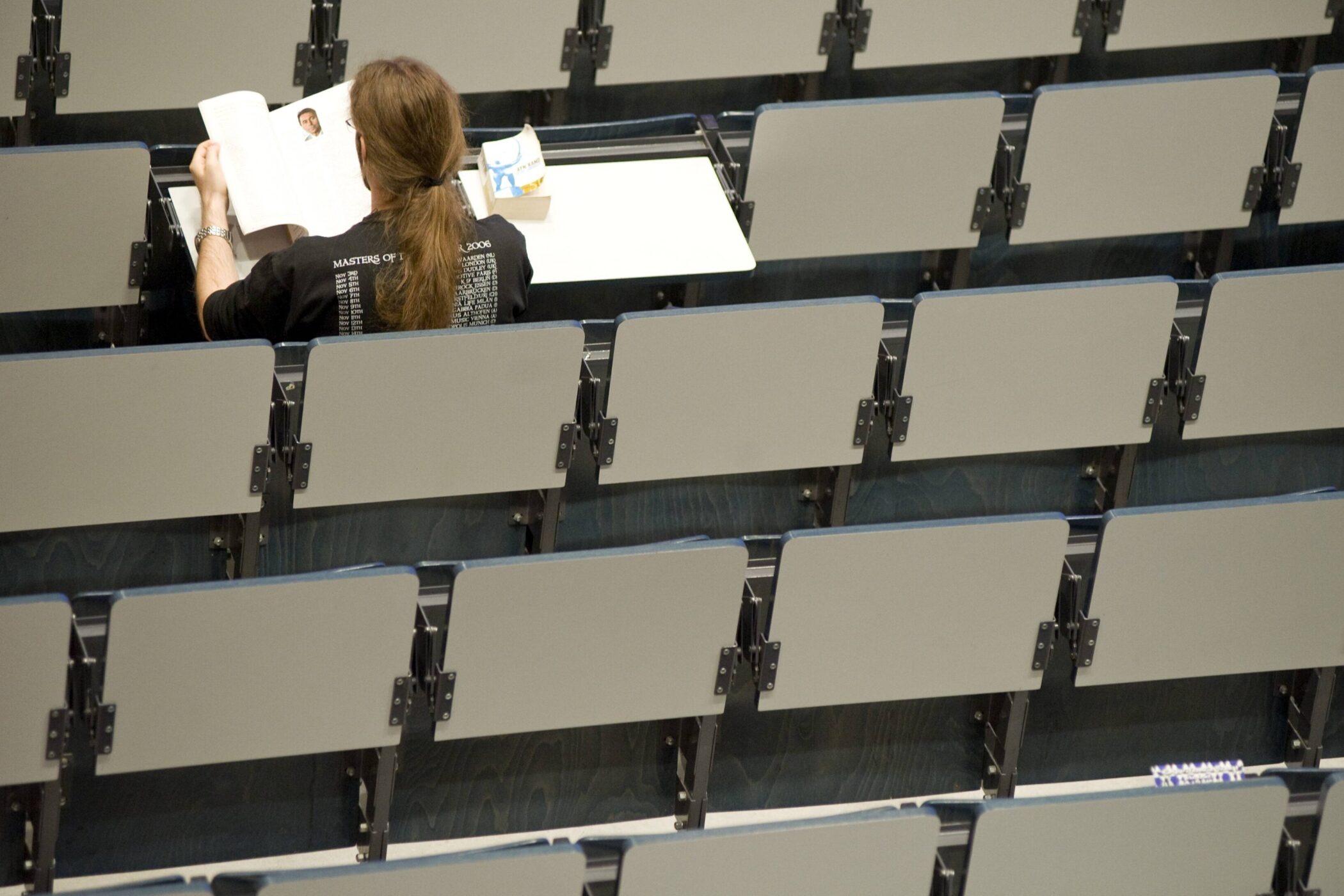 Person sitzt allein in einem Hörsaal und liest ein Buch.