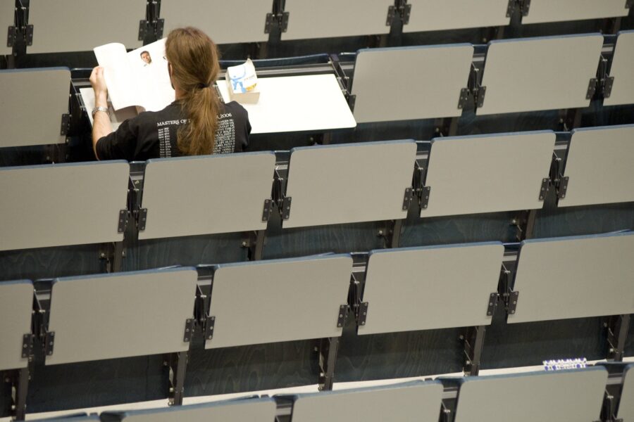 Person sitzt allein in einem Hörsaal und liest ein Buch.